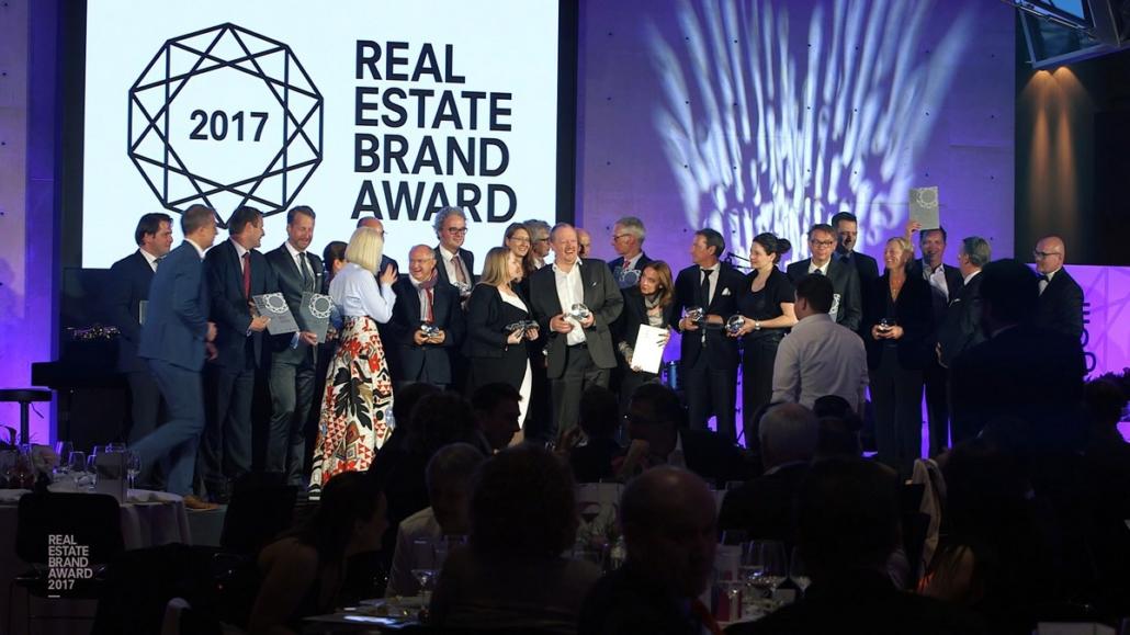 The picture shows in long shot all participants of the Real Estate Brand Awards 2017 on a stage as part of the event documentation.