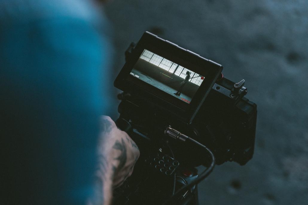 Film production company berlin camera operator photographed over the shoulder, showing the display of his RED-camera with the protagonist in a wide shot in front of a factory wall with windows