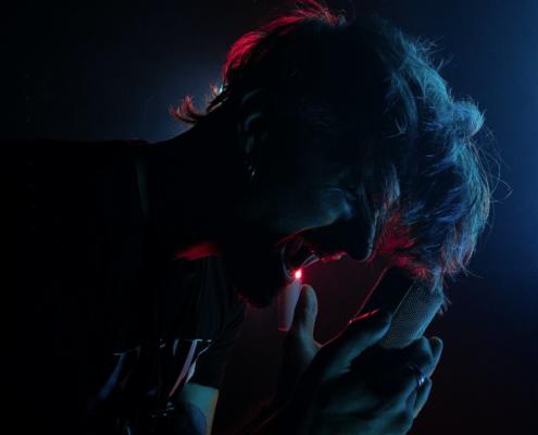 In the picture we see the face of a front singer bent forward, centered in the picture and in profile. Against a dark background we see him singing powerfully into his microphone. From the background he is illuminated by a red neon tube. If you want to create a music video, this image is a good inspiration.