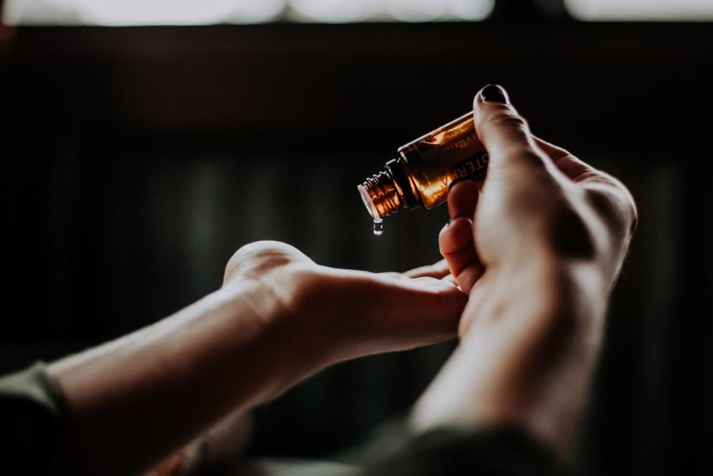 Create a product video of a beauty oil. As an example, a close-up is shown here, in which the hands of a middle-aged woman can be seen in front of a blurred, dark background. With one hand, the woman drips a drop of beauty oil from a dark brown bottle onto the palm of her other hand.