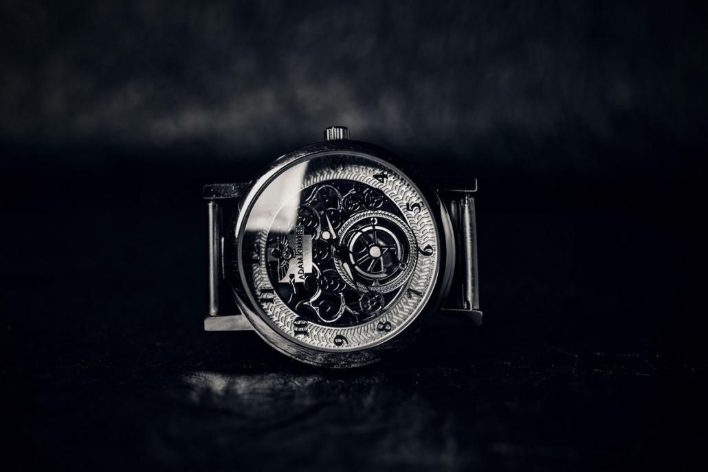 In close-up, we see the filigree, metal dial of a luxurious clock in the center of the image against a black background. The clock lies on a black, strongly reflecting background, in which a kind of mist is reflected, which can also be seen in the background. The scene is in black and white and the glass of the clock reflects light in an impressive way. This is an impressive way to have a TV spot created.