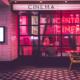 In the picture, the entrance of a red-lit cinema can be seen in a cutaway as a place where the 10 best movies of 2022 can be consumed excellently. The cinema is equipped with a large glass facade and a typical white advertising sign that reads 