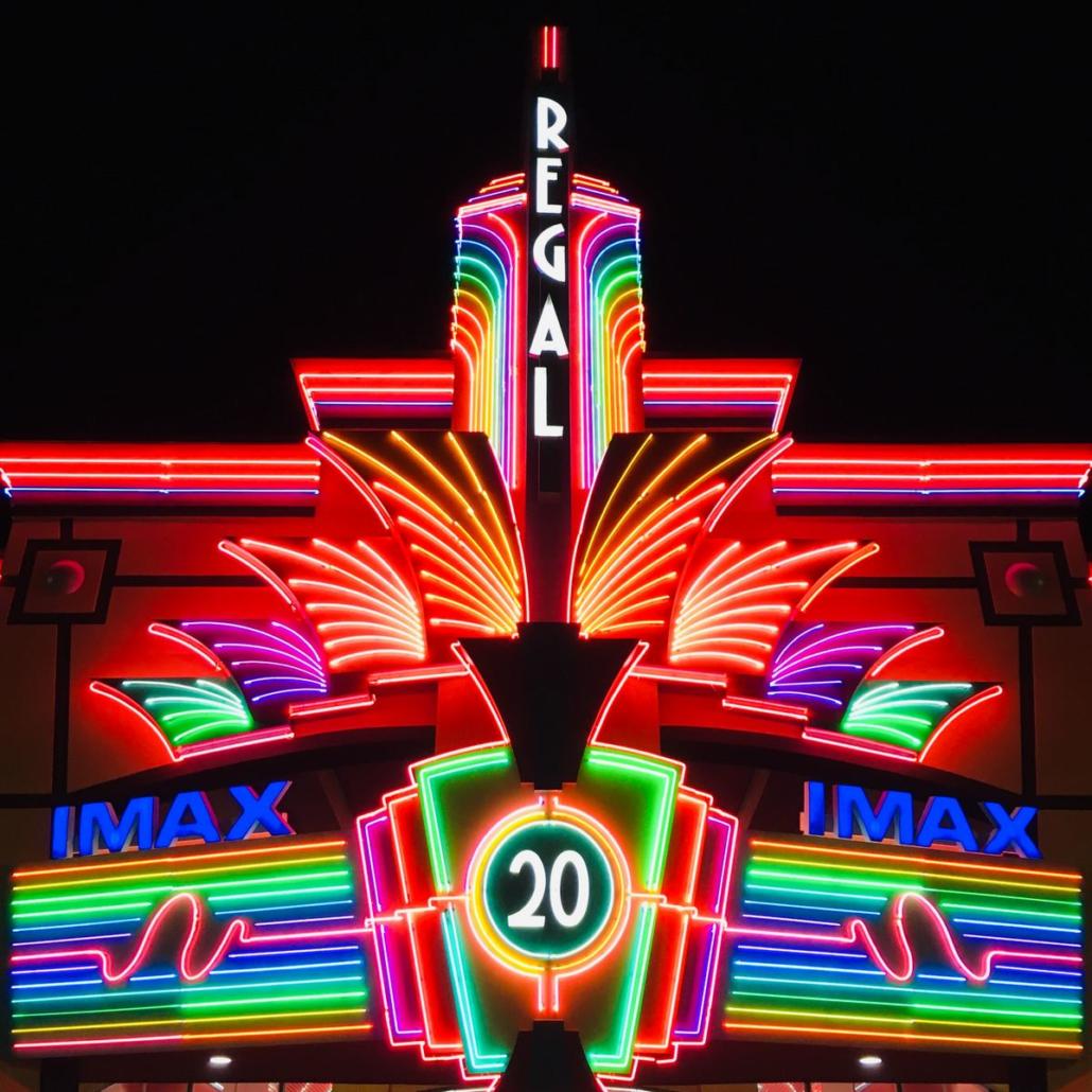 Shown is the very colorfully lit entrance of an IMAX cinema at night. Arranged vertically is the word 