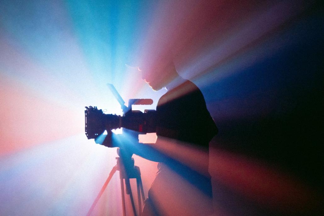 For a video production in Berlin, interesting light setups can be useful, as shown here: We see a cameraman standing at his camera and at the same time in an imposing backlight of red and blue color.