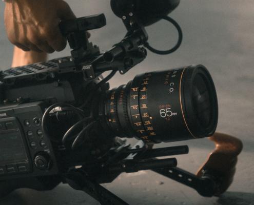 This picture shows a rigged professional camera placed on the floor. We see the hand of the cameraman of a video agency, as he is about to pull up the camera with a handle.