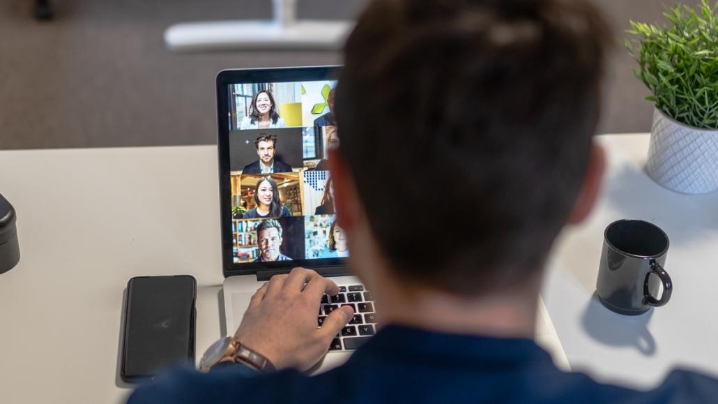 From behind, a crew member can be seen sitting in front of a laptop and participating in an online meeting.